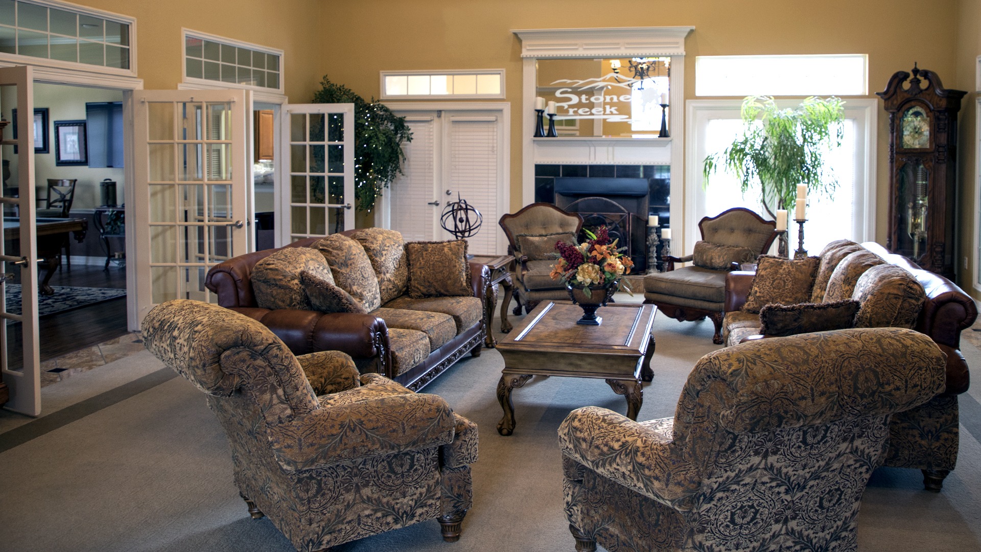 Interior of Stone Creek Apartment Welcome Center lobby with comfortable couches and chairs set up with a fireplace and mirror behind